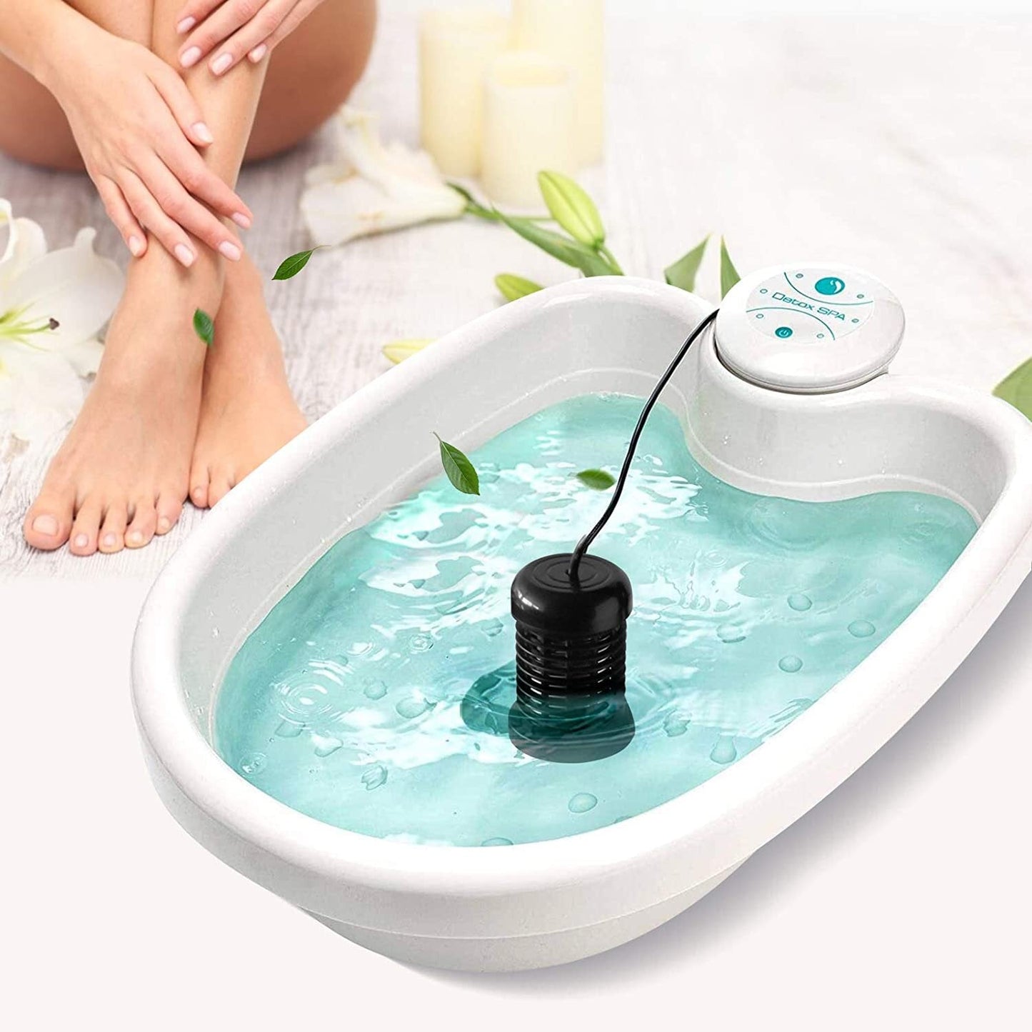 Foot bath with water and a black pump, surrounded by white flowers and a candle.