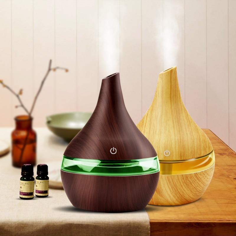 Two diffusers, one brown with green light and one wooden, on a table with essential oils.
